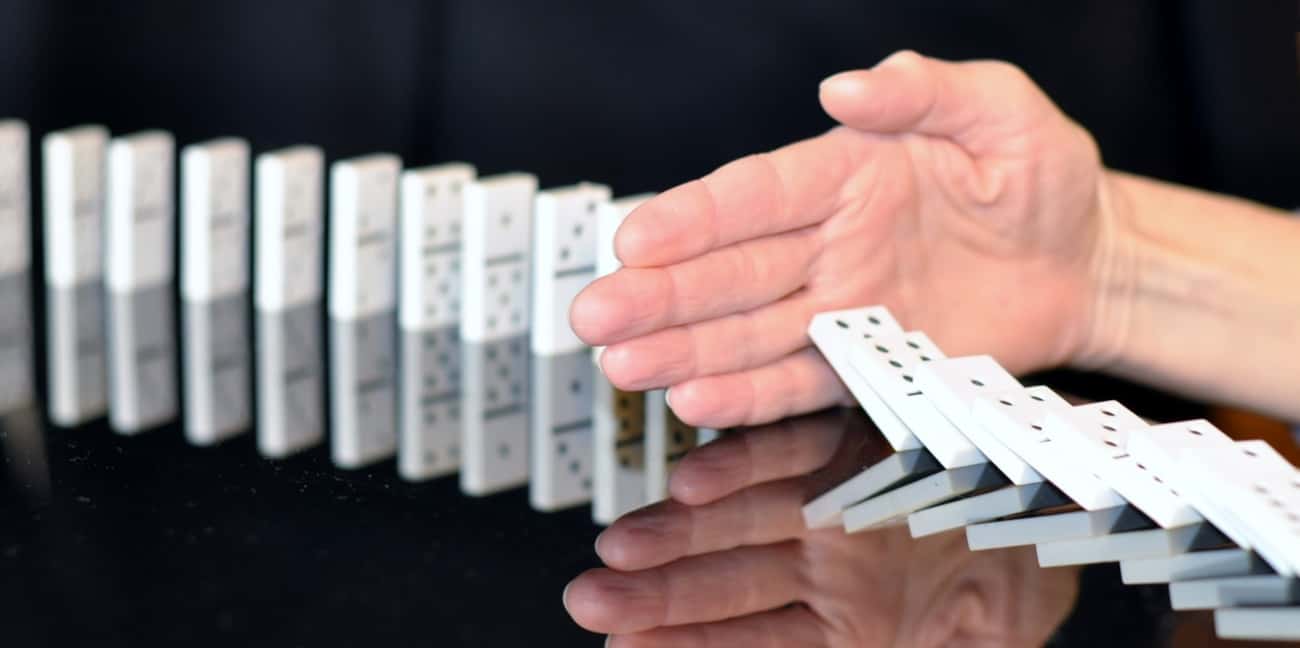 A row of falling dominoes is stopped by a hand