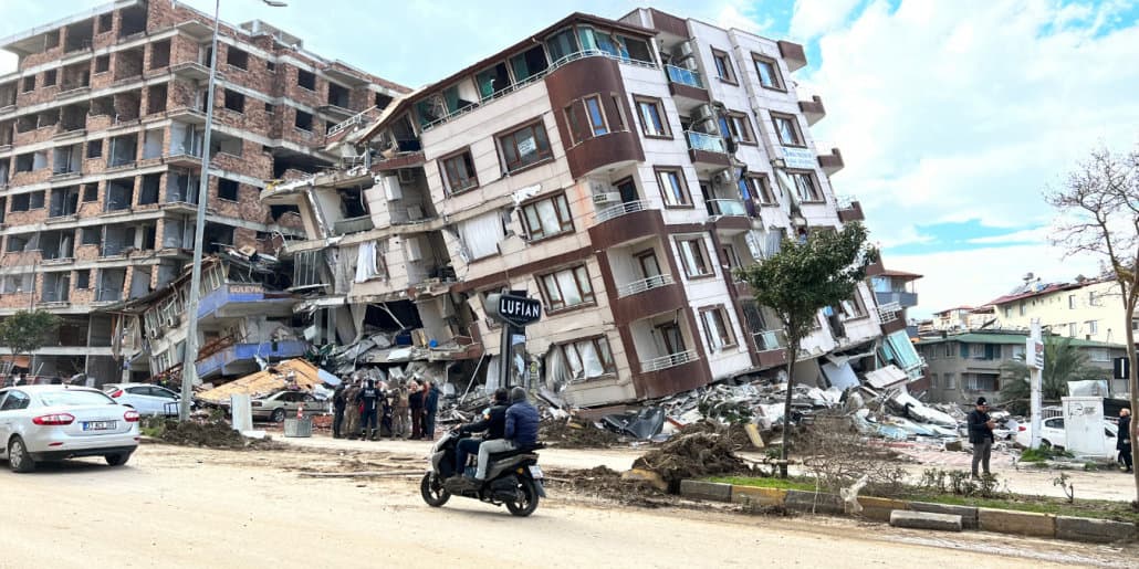 A person on a motorbike drives past a collapsed building