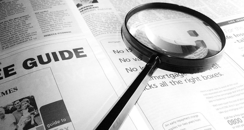 A black and white photo of a magnifying glass lying on a newspaper page.