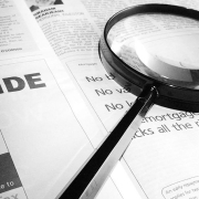 A black and white photo of a magnifying glass lying on a newspaper page.